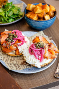A food spread featuring bagels with cream cheese and lox, potatoes and salad.