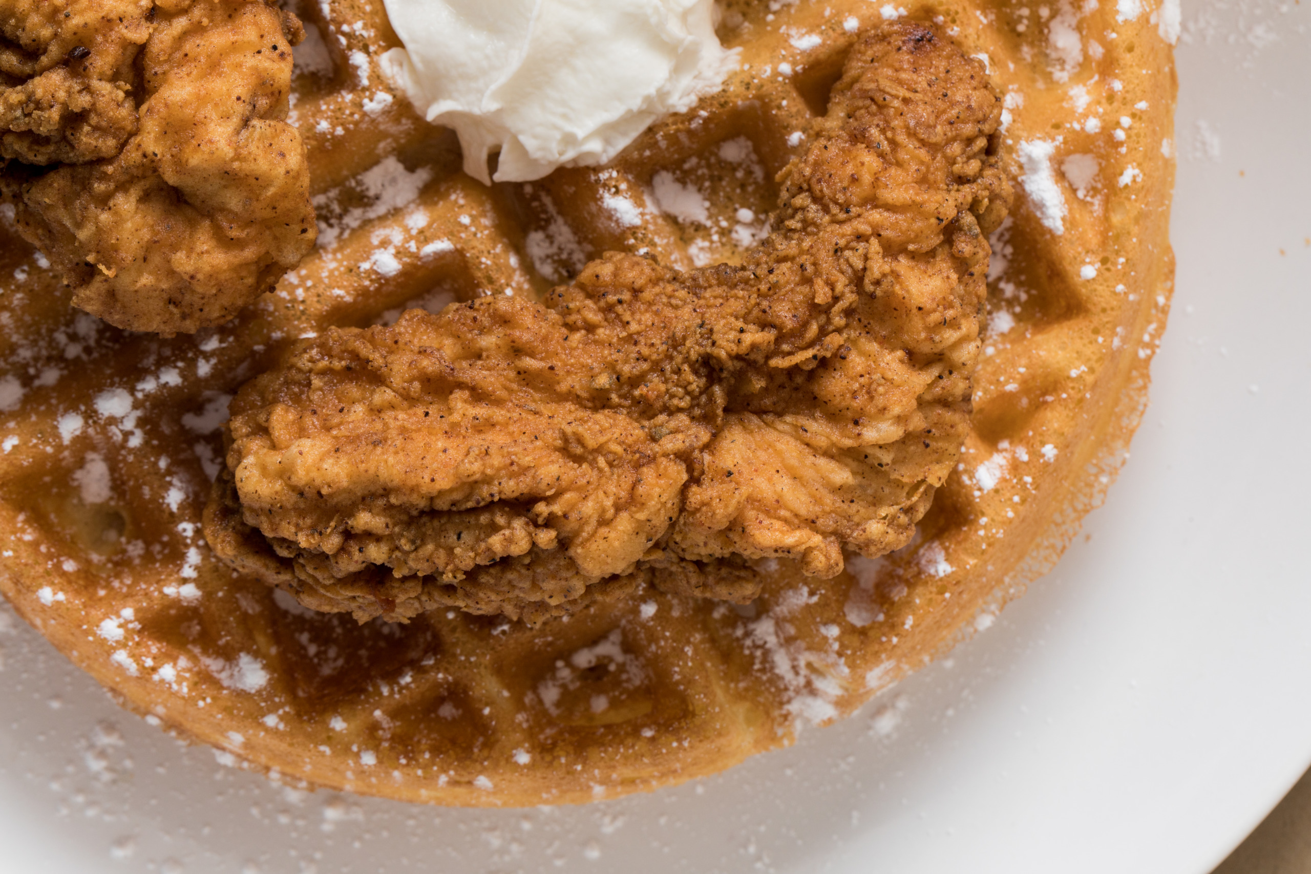 A plate of fried chicken and waffles topped with whipped cream
