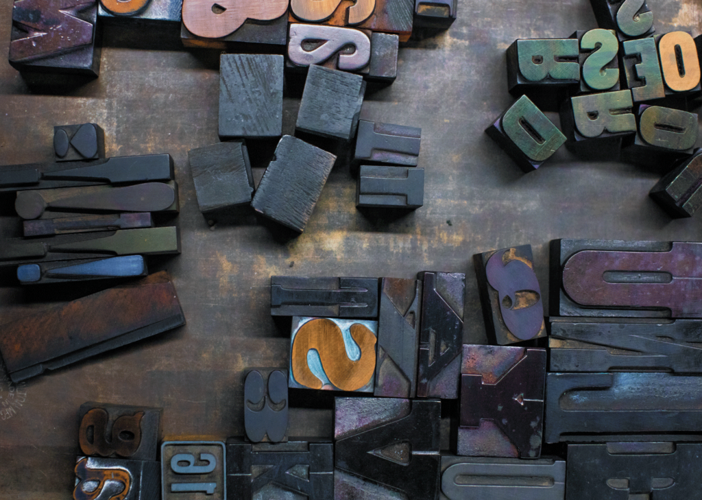An aerial view of wooden letter stamps on a wooden table. The stamps are all made from a dark wood and show different letters.
