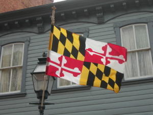 Maryland flag hanging outside a home. The flag has four squares with two alternating patterns. The first pattern is yellow and black diamonds. The second pattern is white and red crosses.