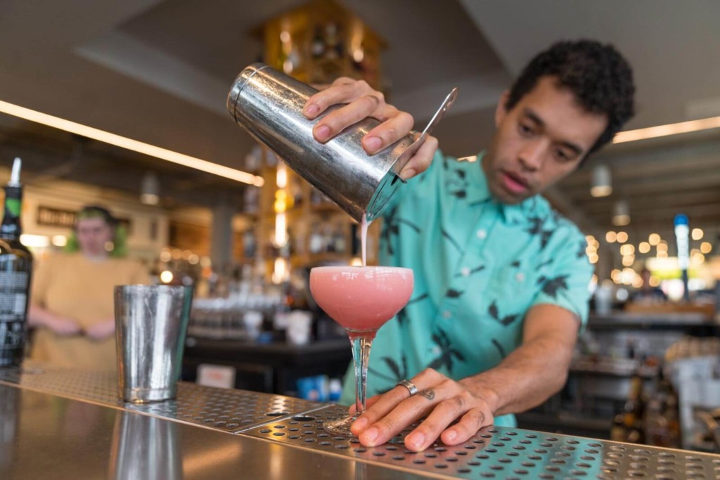 A bartender strains a pink cocktail into a martini glass at Rbar