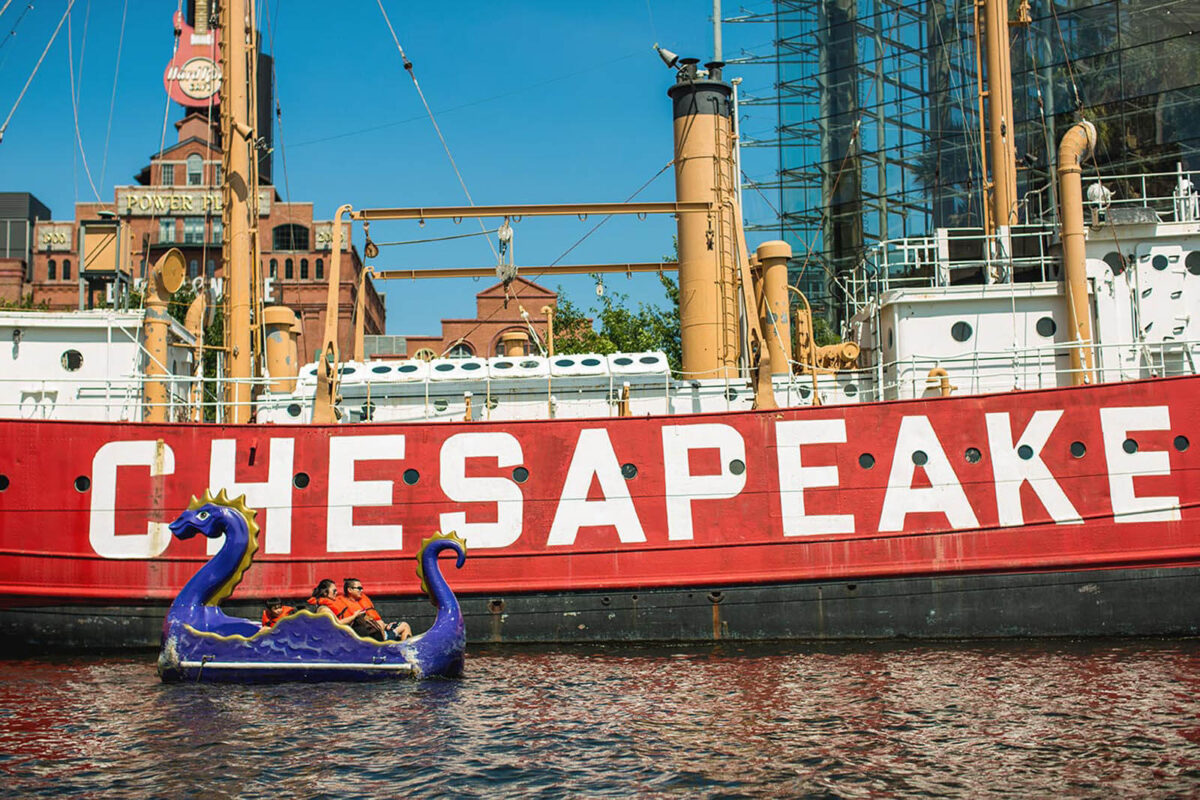 Three people in a dragon boat in from of The Chesapeake Boat in The Inner Harbor in Baltimore.