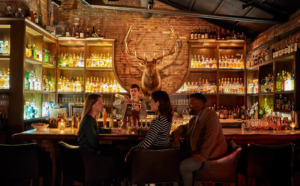 Three customers sit at the bar while the bartender makes drinks at The Elk room interior in Baltimore.