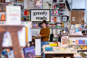 Greedy Reads Bookstore employee standing among books