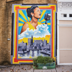 Mural of Billie Holiday singing into a microphone with the Baltimore skyline under her