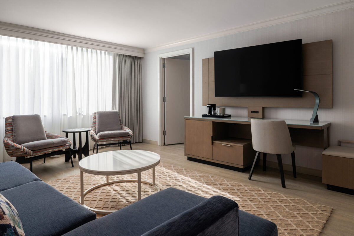 The newly renovated Junior Suite living room offers a spacious and inviting retreat featuring contemporary furnishings, a comfortable seating area, elegant design details, a dedicated workspace, and a 65-inch Smart TV with streaming capabilities. Perfect for relaxing, working, or entertaining.