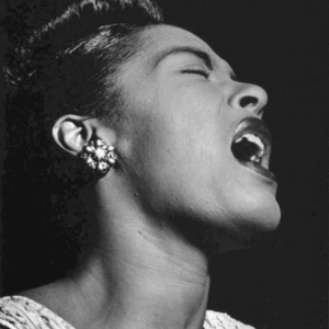 Black and white portrait of Billie Holiday, mouth open, as she sings. 