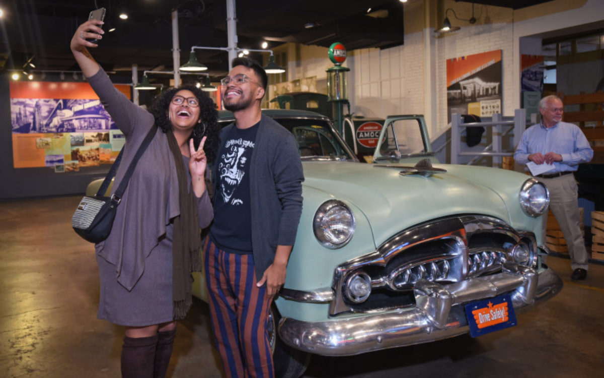A man and woman take a selfie in front of a vintage car