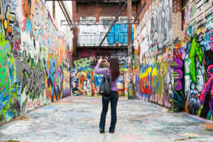 A woman takes a photo of an alley covered in colorful and artistic graffiti