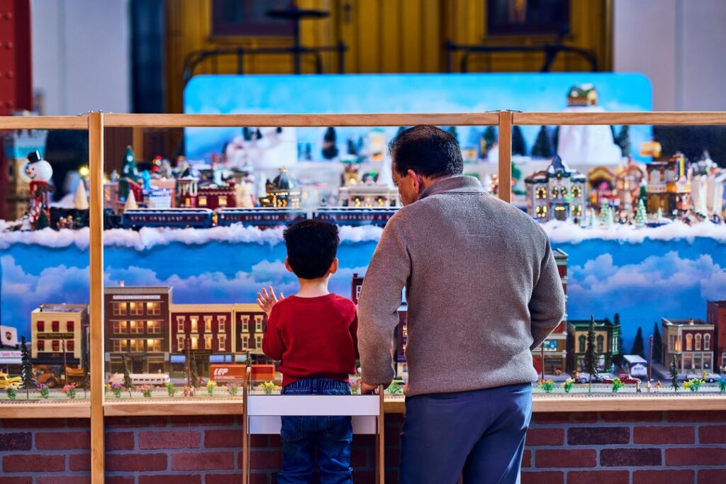 A young boy and his grandpa look at a train set
