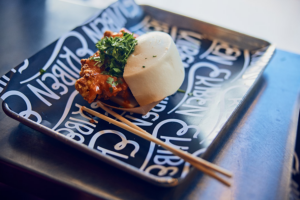 A bao bun and chopsticks rest on metal serving tray