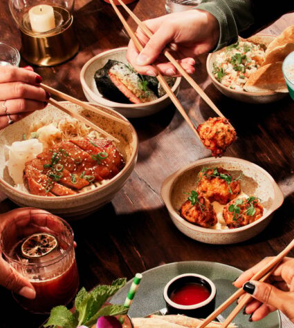 Hands holding chopsticks hover over small plates