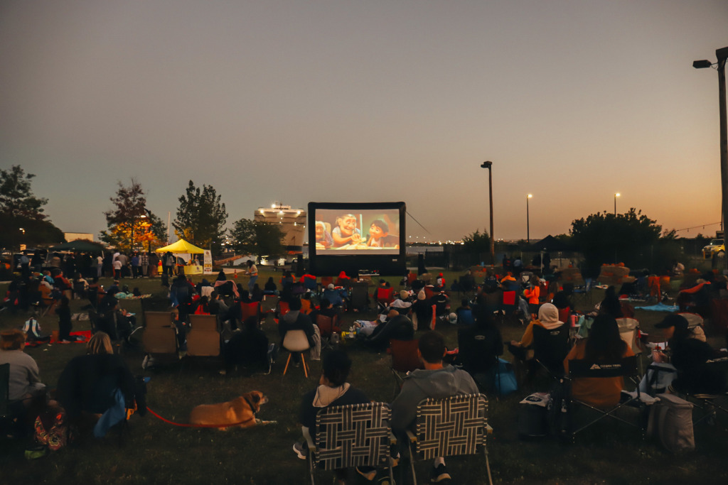 a crowd gathers to watch an outdoor movie at dusk