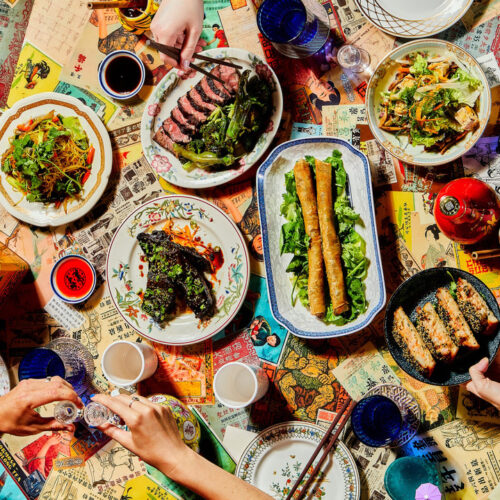 An overhead shot of hands reaching toward colorful food and drinks on a busy table