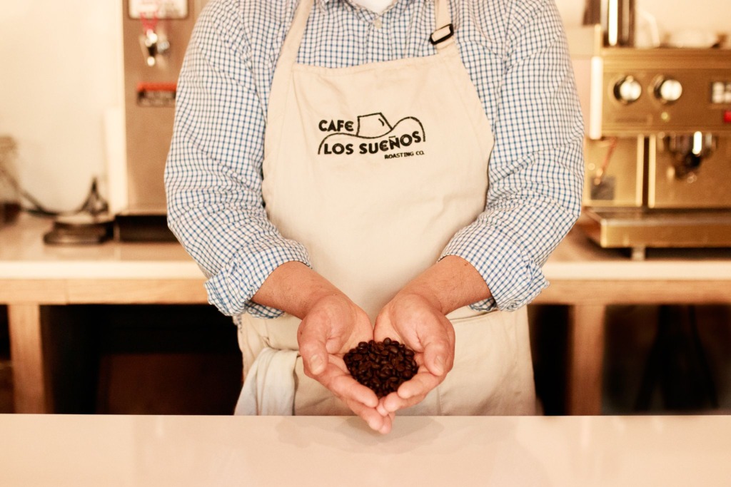 Man wearing an apron poses with a scoop of coffee beans in his hands