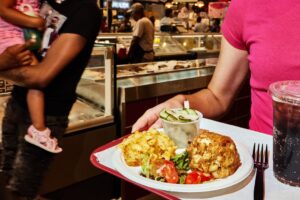 a woman holds a tray with a crab cake and sides