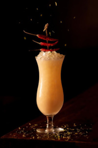 An orange cocktail with peppers on top