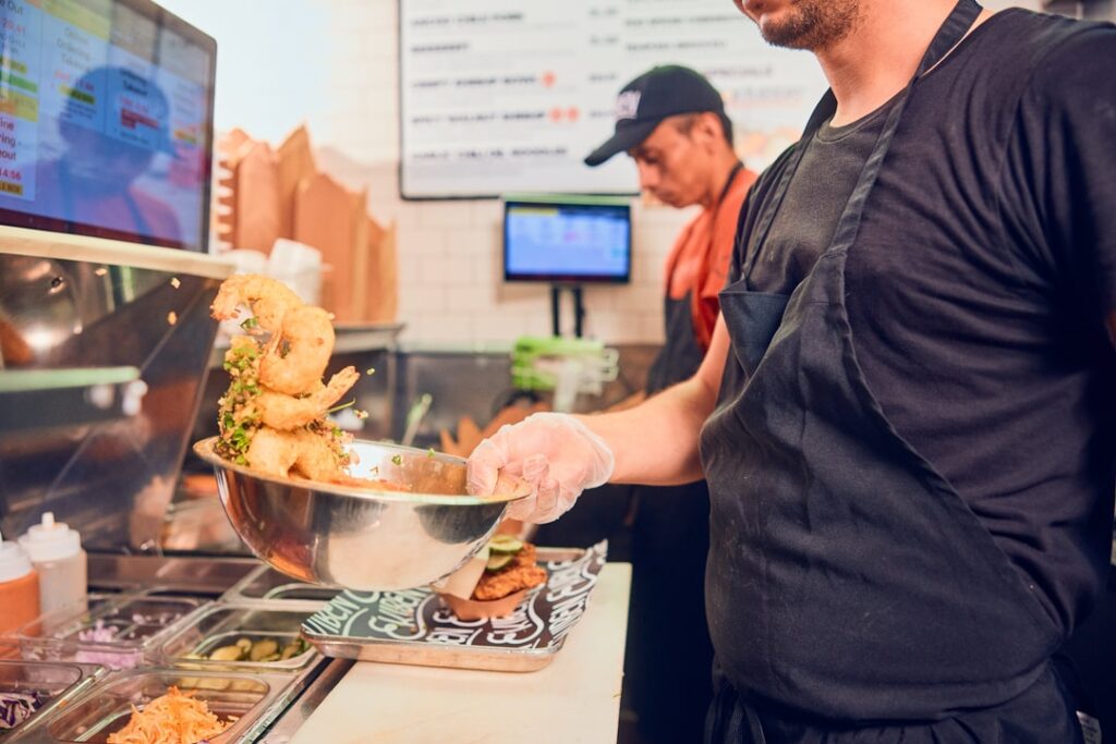 A man wearing gloves and an apron tosses fried shrimp with seasonings
