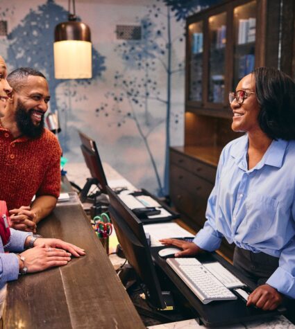 Two people at a hotel front desk talking to someone behind the desk