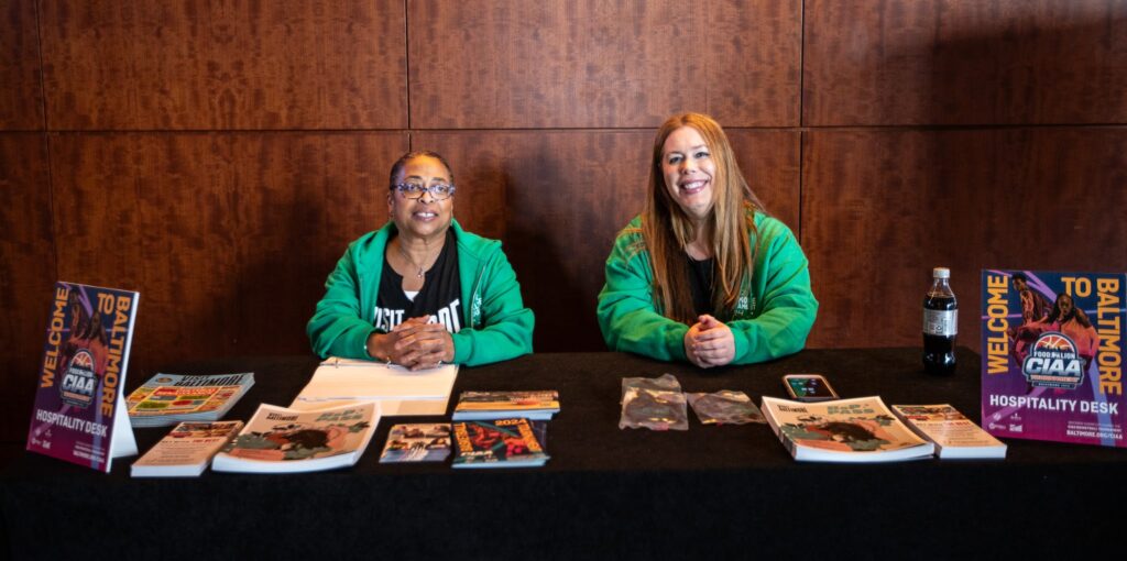 Two women in matching sweatshirts sit behind a table
