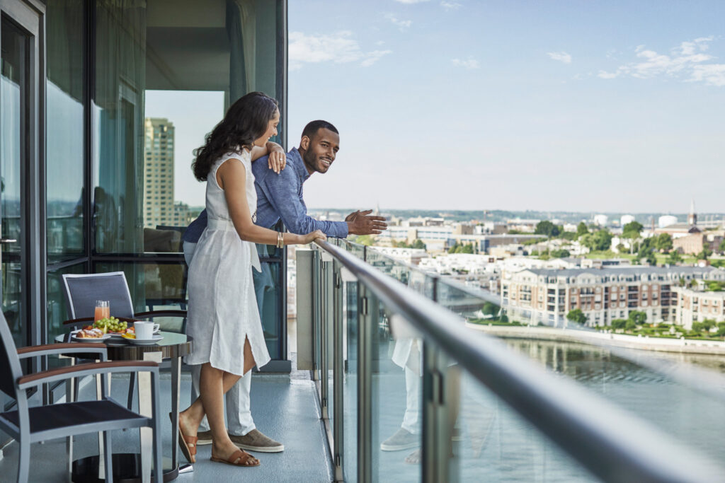 A woman and a man look over a balcony at the water 